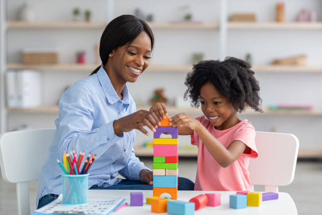 Little girl and child development specialist playing with colorful wooden bricks.